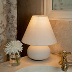 Small ceramic bedside lamp with a white linen shade styled in a warm neutral bedroom interior.