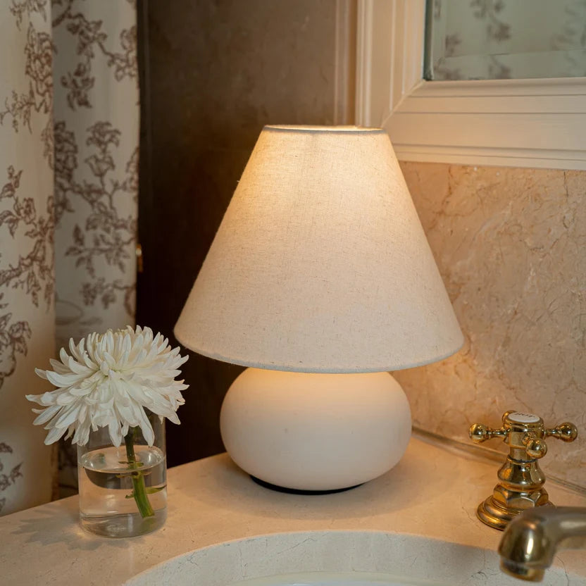 Small ceramic bedside lamp with a white linen shade styled in a warm neutral bedroom interior.