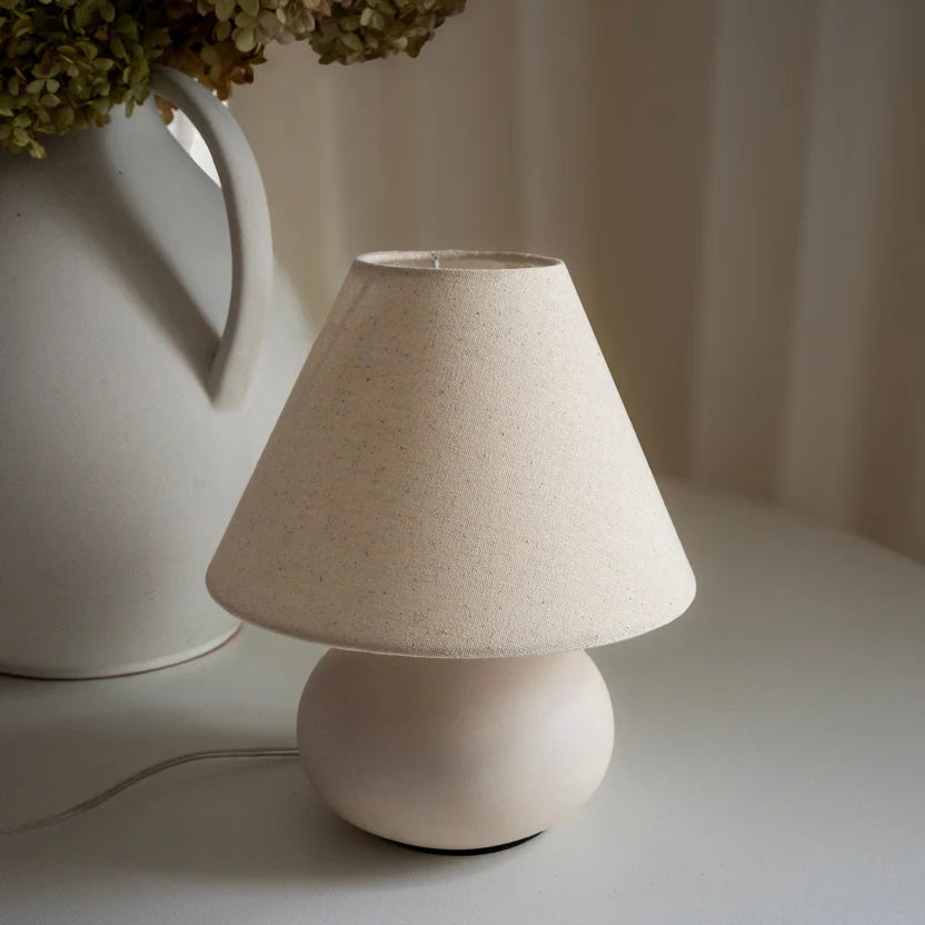Cream ceramic table lamp with a linen shade styled in a softly lit neutral interior.