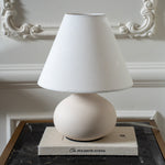 Cream ceramic table lamp with a linen shade styled on a black marble side table against decorative wall moulding.