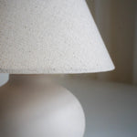 Close-up of the white linen lamp shade and softly rounded cream ceramic base.