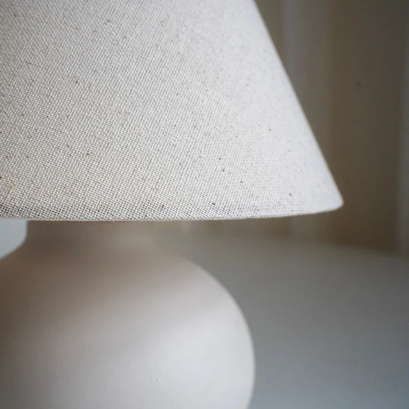 Close-up of the white linen lamp shade and softly rounded cream ceramic base.