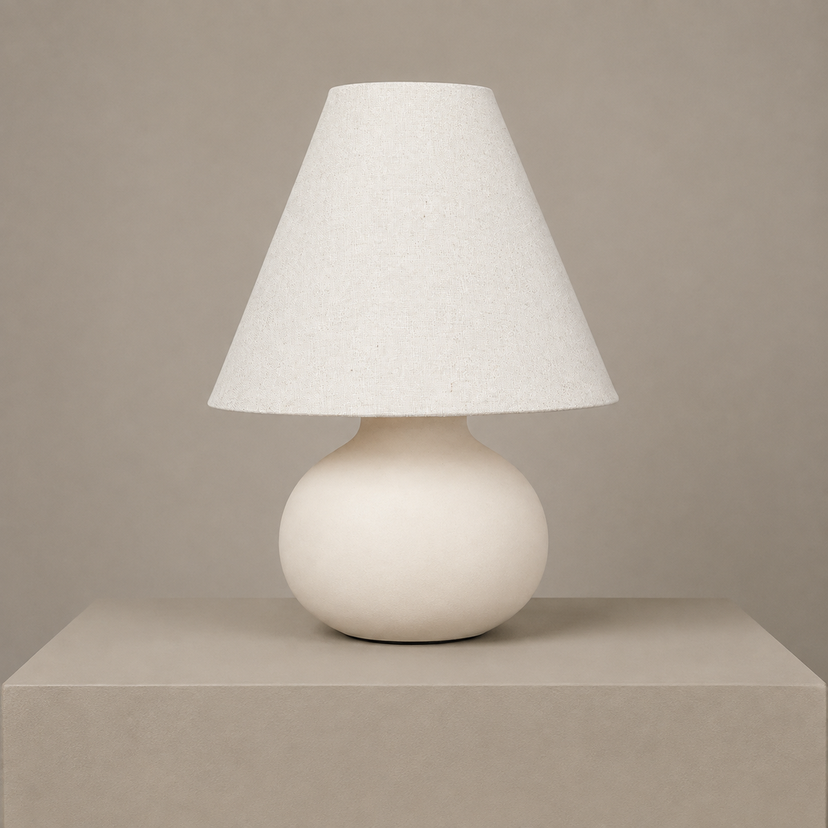 Small cream ceramic table lamp with a rounded base and white linen shade on a neutral studio backdrop.