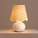 Illuminated ceramic table lamp with a woven shade casting a warm, diffused glow