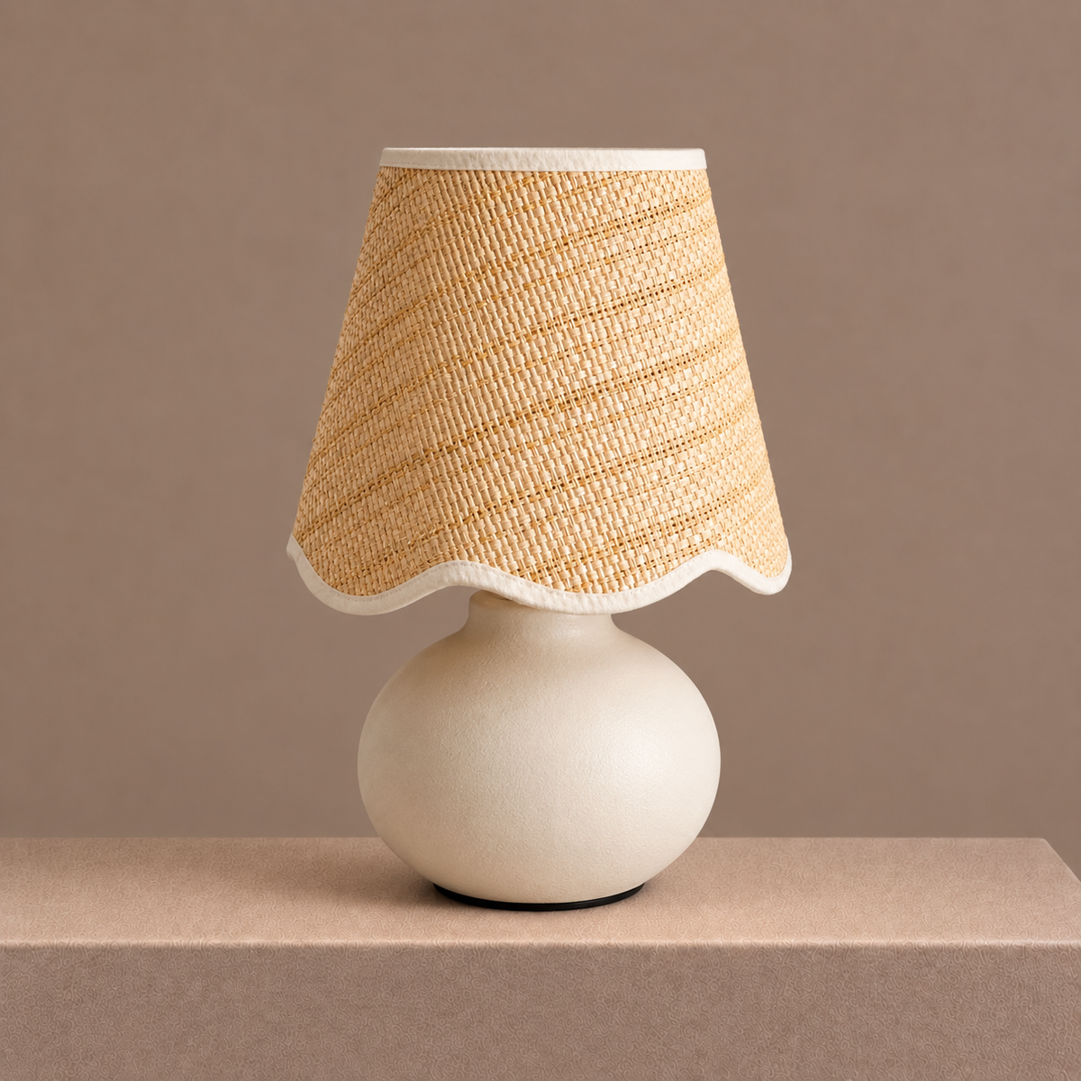 Small ceramic table lamp with a rounded cream base and softly scalloped woven shade on a neutral pedestal.