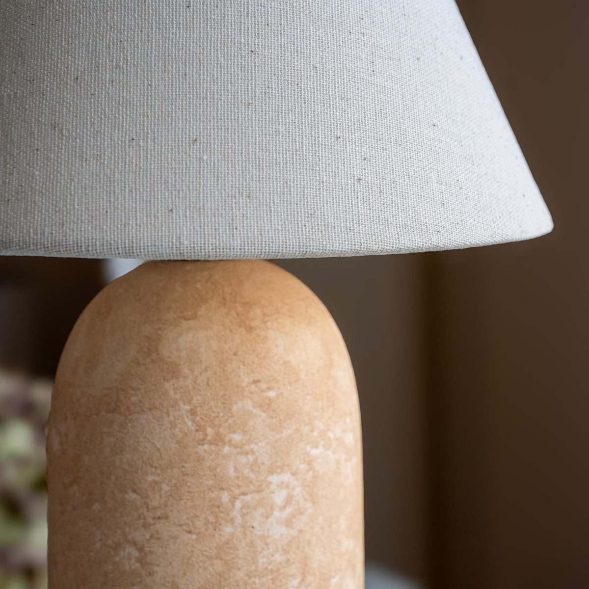 Close-up of the linen lamp shade and textured sandstone base in a softly lit interior.