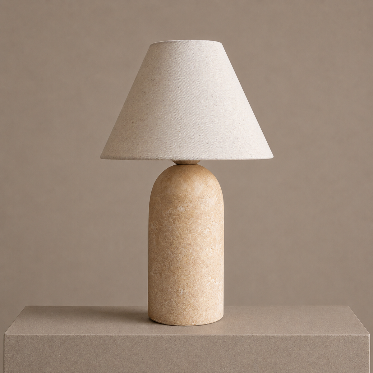 Small sandstone table lamp with a textured cylindrical base and soft linen shade on a neutral pedestal.
