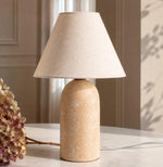 Sandstone and linen table lamp styled beside a window in a warm neutral interior.