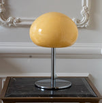 Cream mushroom table lamp with chrome base styled against ornate wall moulding in a neutral interior.