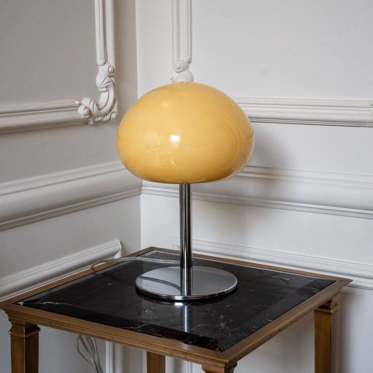 Small cream glass table lamp styled on a dark marble side table in a classic interior.