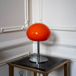 Orange mushroom table lamp with chrome base styled against ornate white wall moulding in a classic interior.