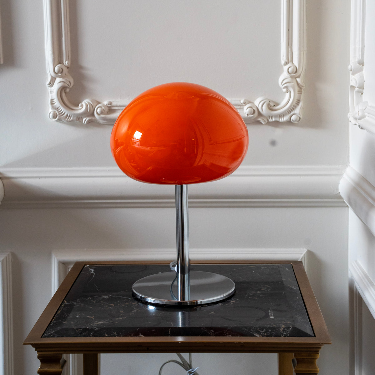 Orange glass mushroom lamp styled on a dark marble side table in a softly lit interior.