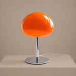Orange glass mushroom table lamp with a chrome stem and round base styled on a neutral pedestal.