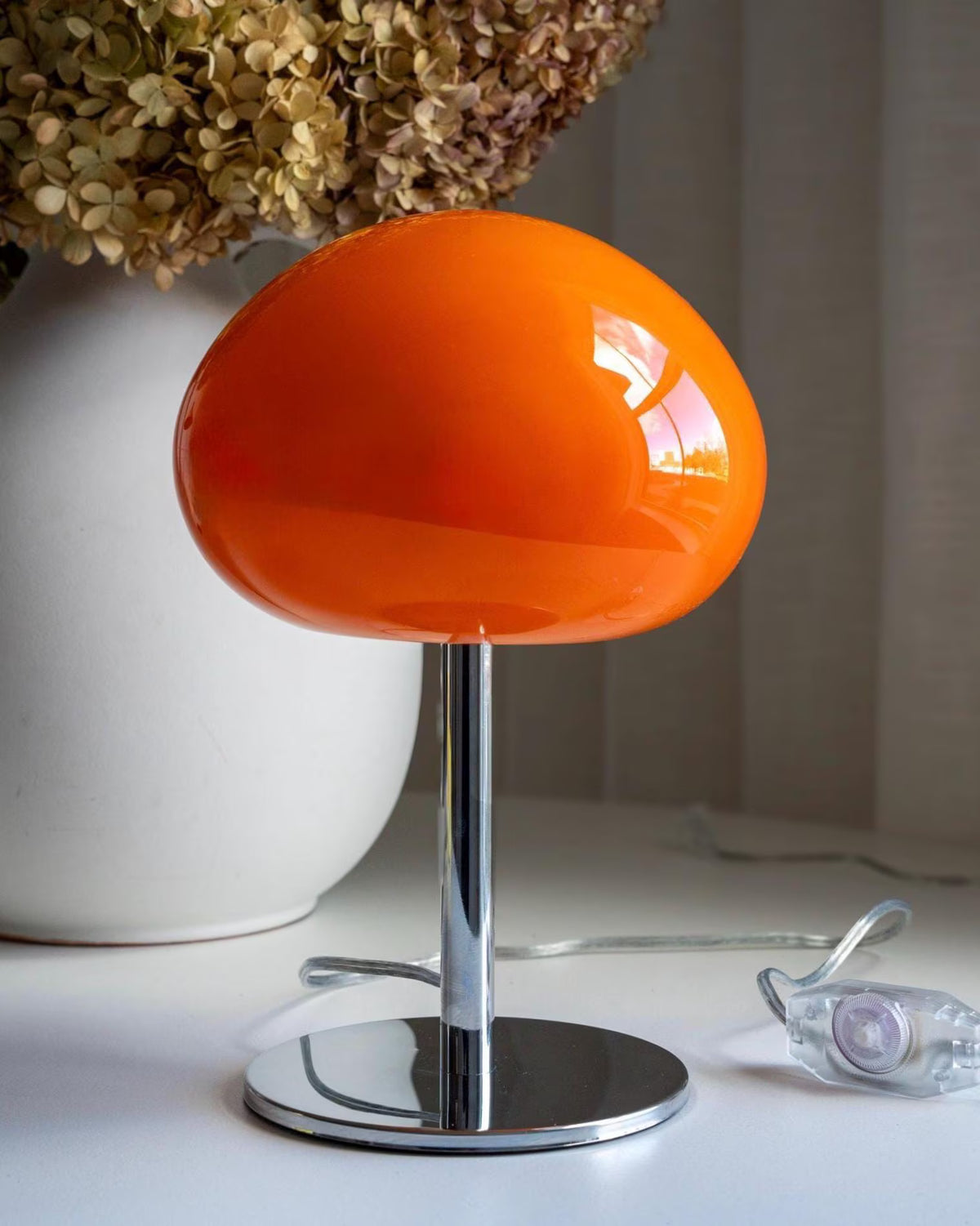 Sculptural orange glass table lamp styled beside a window with a polished chrome base