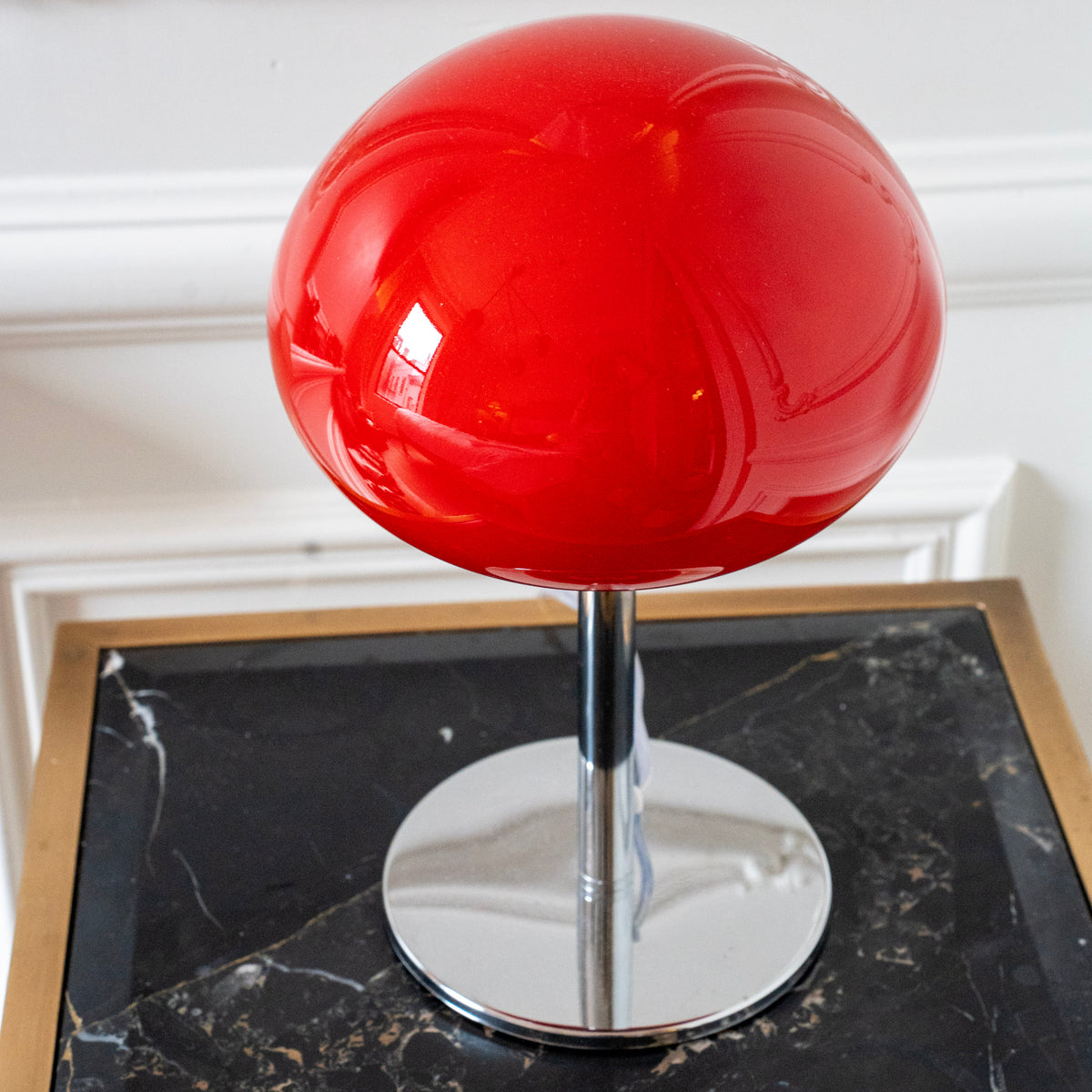 Close-up of a glossy red glass mushroom shade with polished chrome stem and base styled on a black marble side table.