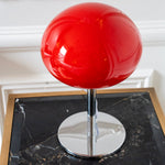 Close-up of a glossy red glass mushroom shade with polished chrome stem and base styled on a black marble side table.