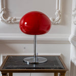 Red glass mushroom lamp styled in a warm modern interior with a sculptural chrome base.