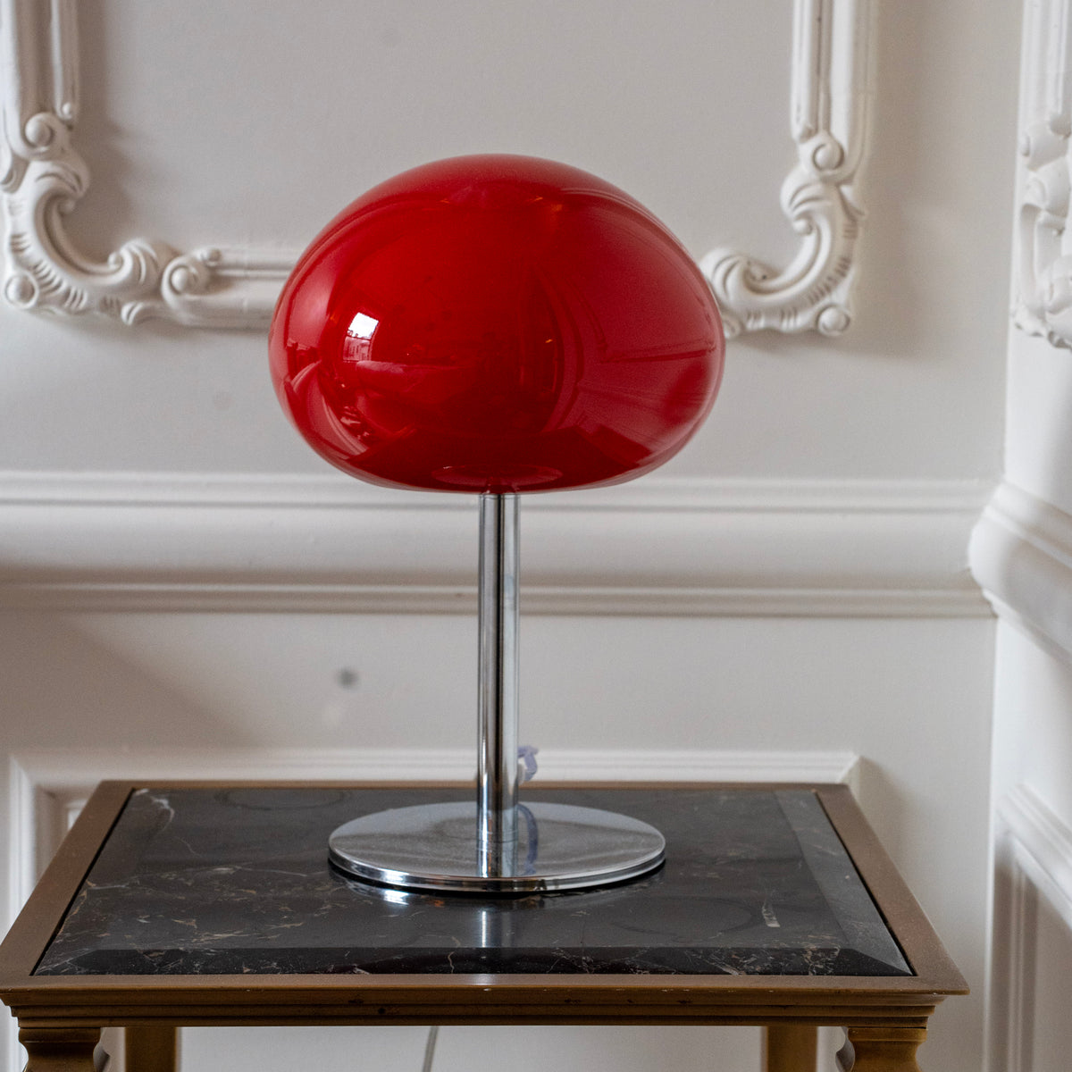 Red glass mushroom lamp styled in a warm modern interior with a sculptural chrome base.