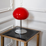 Sculptural red glass table lamp styled on a black marble side table against decorative white wall moulding.