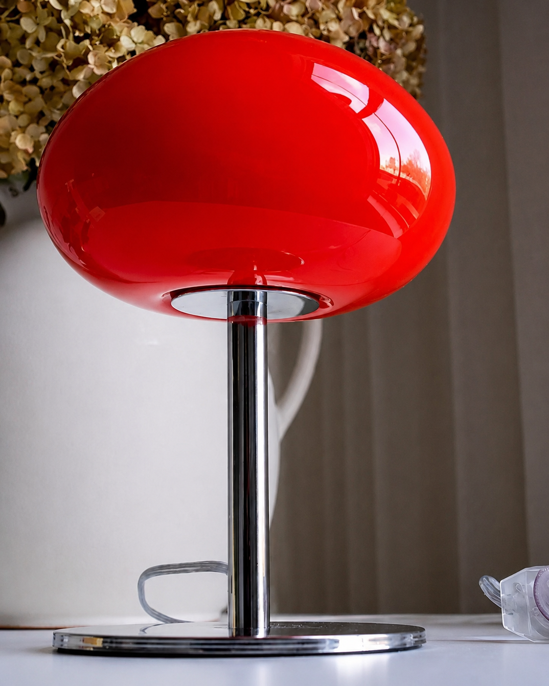 Sculptural red glass shade with a glossy finish above a polished chrome lamp base.