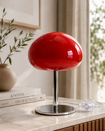 Small red glass table lamp styled beside a window in a bright interior.