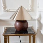 Sculptural woodgrain and brass lamp styled on a black marble side table against decorative wall moulding.