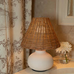 Cream ceramic table lamp with a woven rattan shade styled in a warm, collected interior.