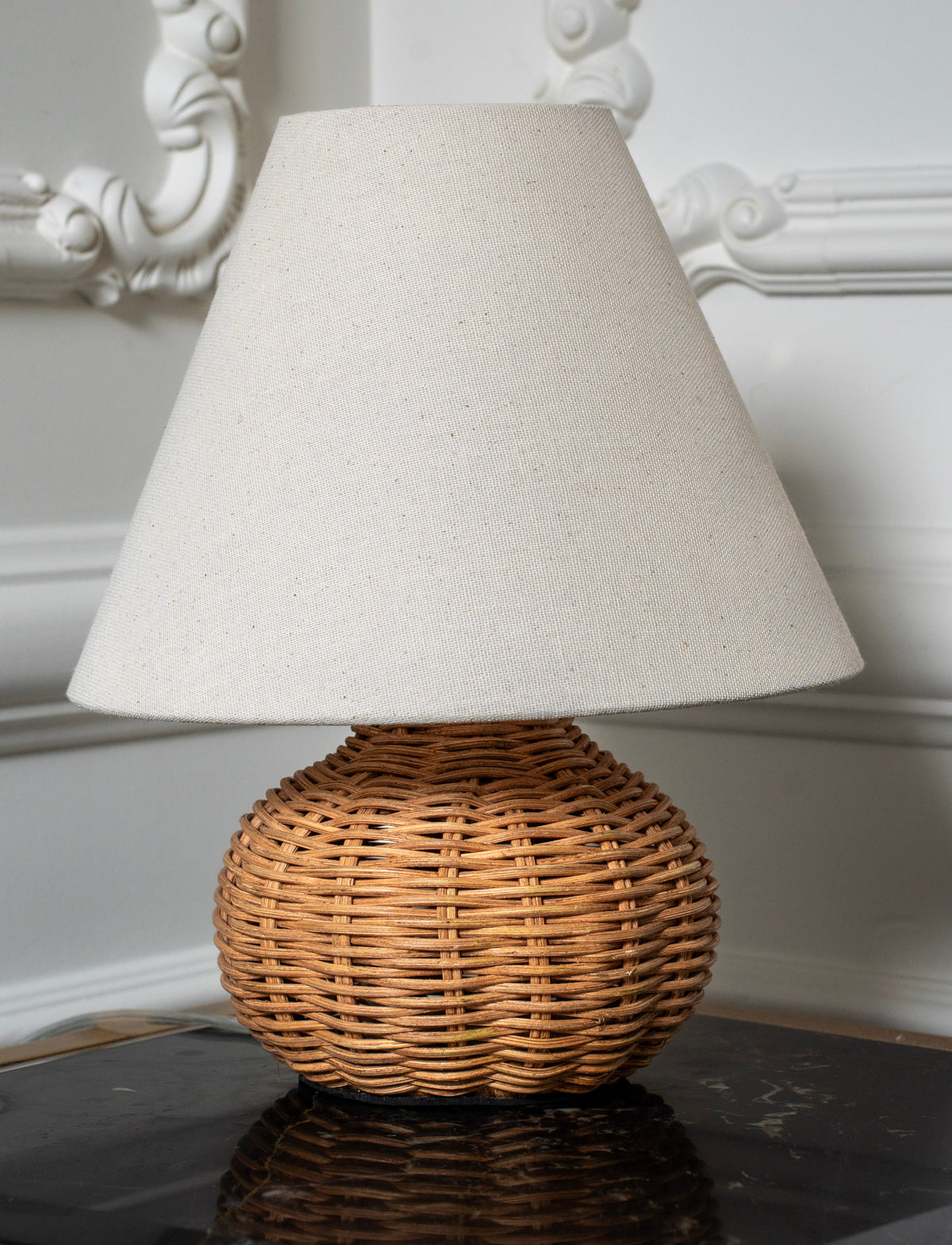 Small woven rattan lamp styled on a book against decorative white wall moulding.