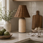 Small rattan table lamp with sandstone base styled on a kitchen counter in a neutral interior.