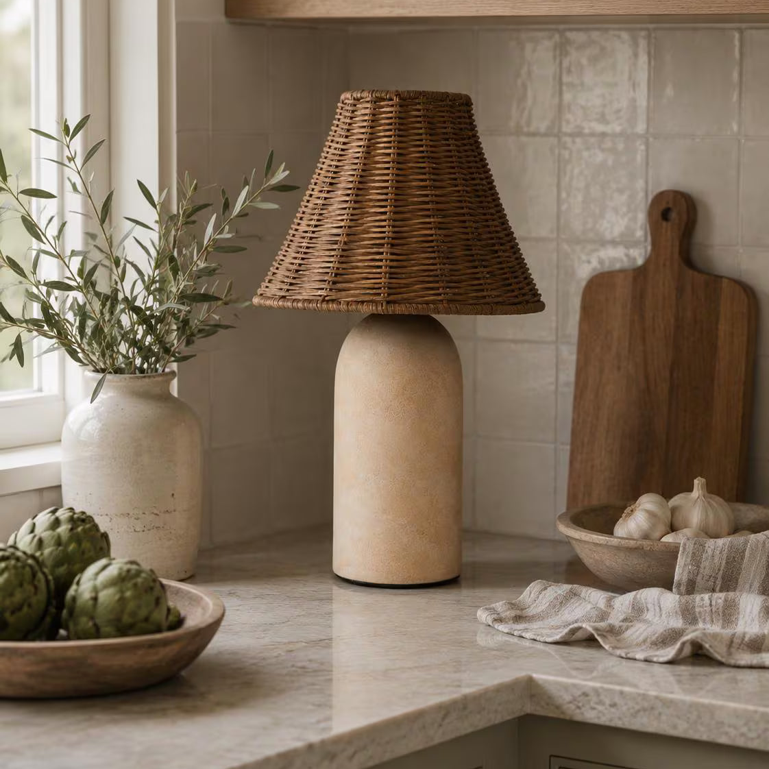 Small rattan table lamp with sandstone base styled on a kitchen counter in a neutral interior.