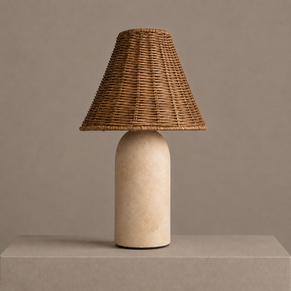 Small rattan table lamp with a sandstone ceramic base and woven shade on a neutral pedestal.