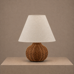 woven rattan table lamp with white fabric shade styled on a neutral pedestal