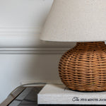 Close-up of The Reed table lamp featuring a handwoven rattan base and textured off-white fabric shade.